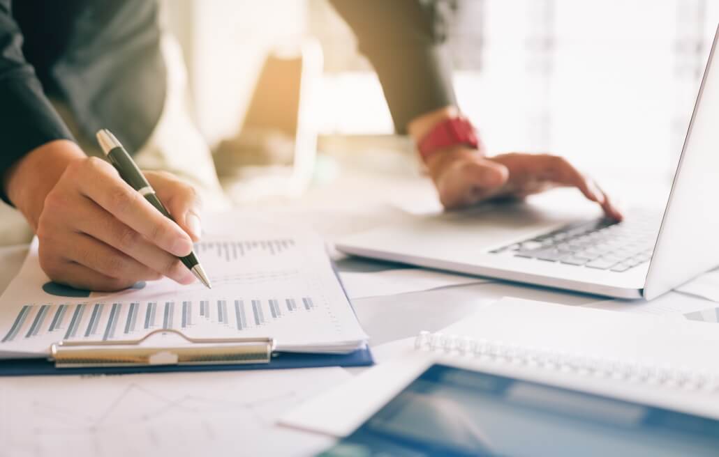 Businessman holding pen and pointing paper chart summary analyzing annual business report with using laptop working from home.