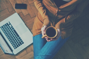 Coffee cup in girl’s hands sitting on a wooden floor