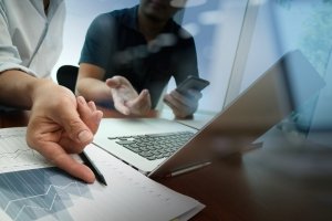 business documents on office table with smart phone and digital tablet and graph business diagram and man working in the background