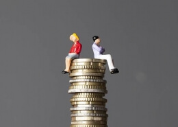 A miniature man and a miniuature woman sitting on top of a pile of coins representing gender equality