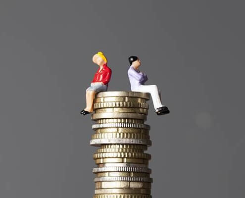 A miniature man and a miniuature woman sitting on top of a pile of coins representing gender equality