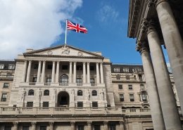 Bank of England facade from below with UK flag and blue sky in the background