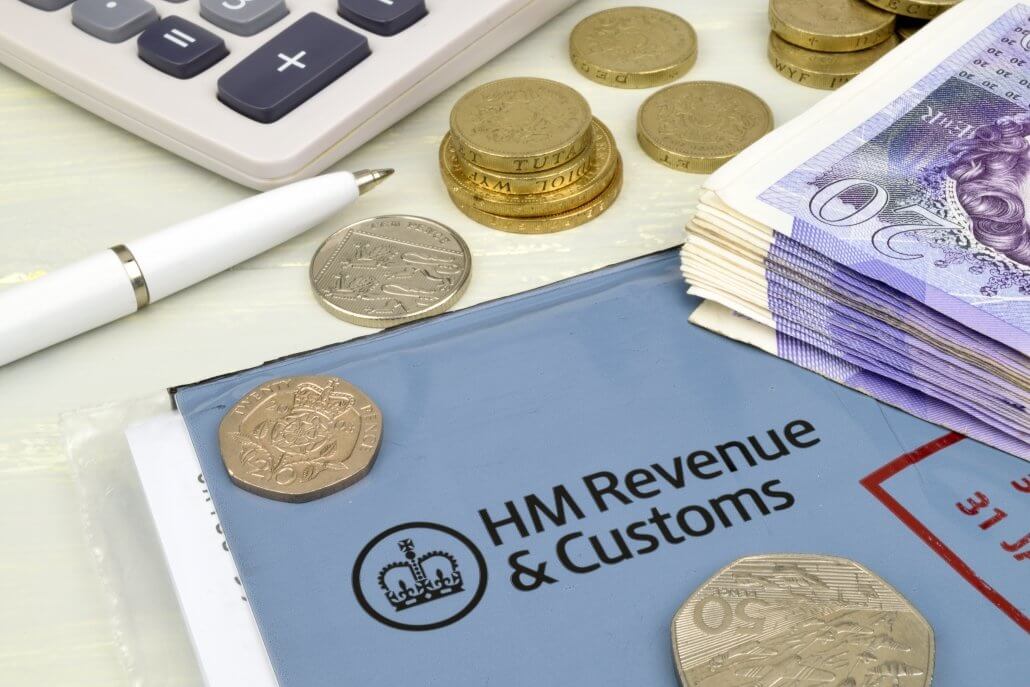 A still life of UK tax return objects, including a calculator, cash and pen, symbolising the finance element to consider when returning to the UK