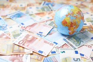 Tiny Earth globe over the surface covered with the multiple bank note bills symbolising the impact of Coronavirus on global growth