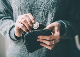 Hands holding British pound coin and small money pouch, symbolising the benefits of returning to the UK