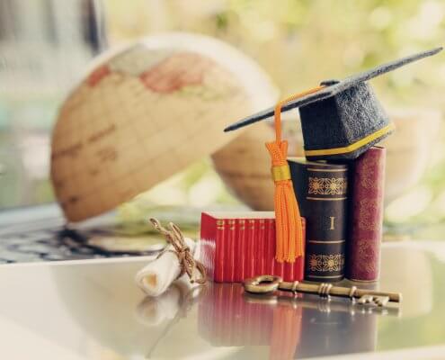 Graduate study abroad program for opening or expand world view concept : Graduation cap or hat, a key, world globe map, foreign text book on laptop, depicts achievement or success in online education