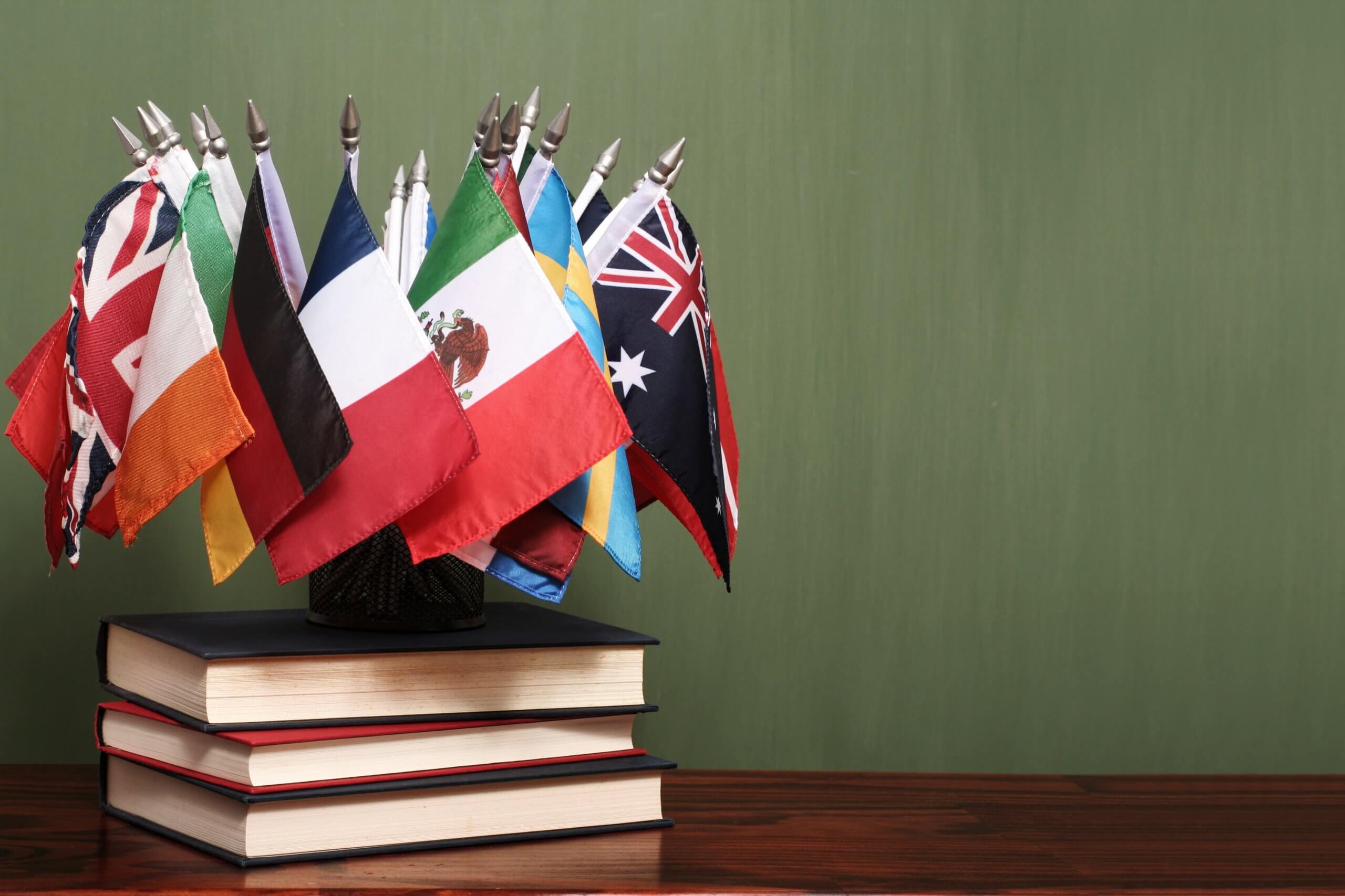 World flags on a pile of books in front of a green chalkboard