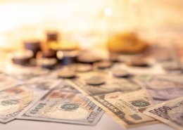 Various of international money coin and banknote with blurred hourglass in the background. Time investment with currency exchange concept. Focus on dollar banknote.