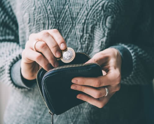 Hands holding british pound coin and small money pouch