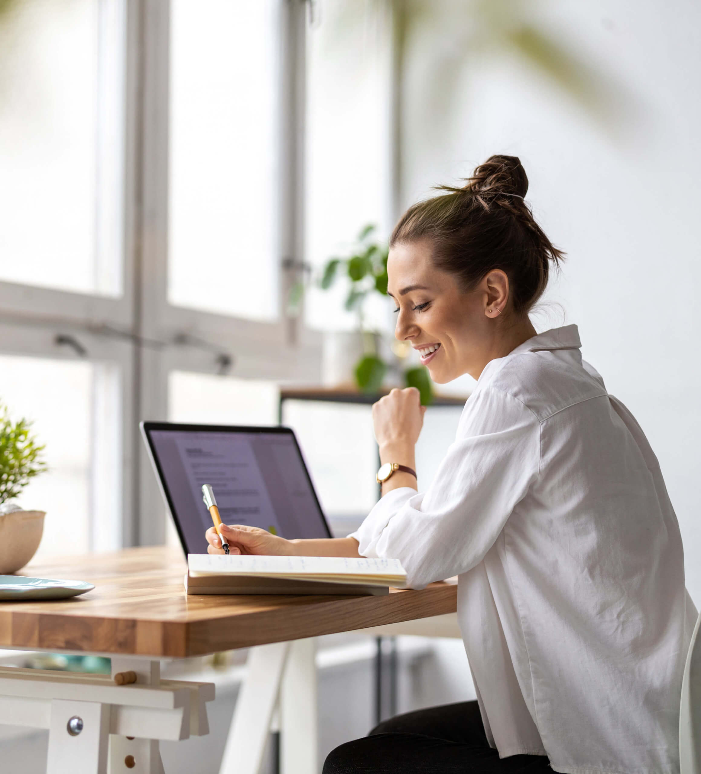 woman in front of the laptop and writing on a book